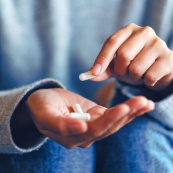 A set of hands holding three white capsules.