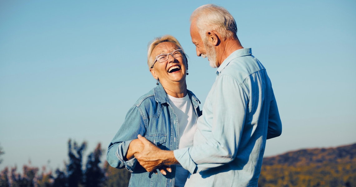 An older aged couple laughing together outdoors.