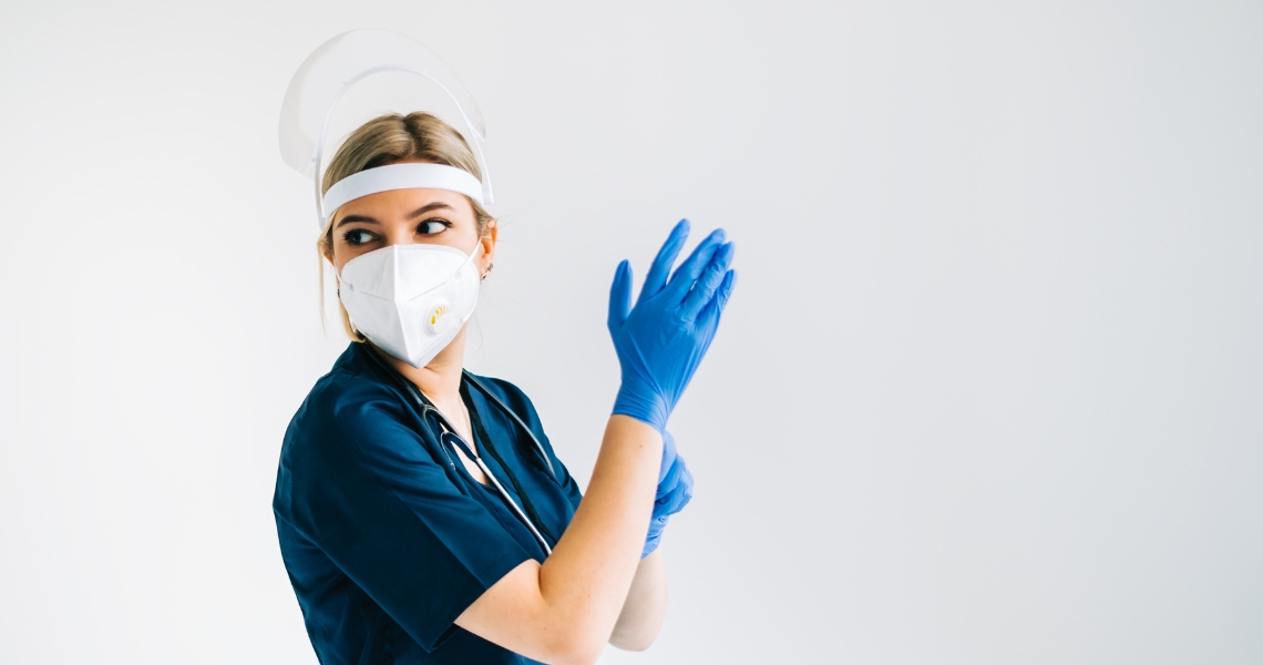 A woman in PPE putting on gloves.