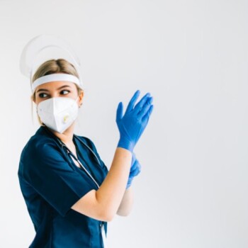 A woman in PPE putting on gloves.