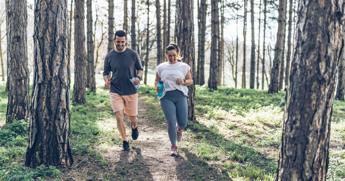 A man and woman running through the forest on a trail.