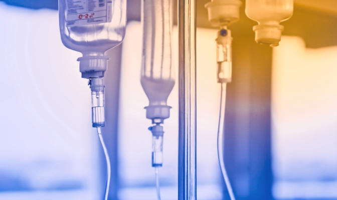A blue and orange toned image displaying IV bags hanging on an IV pole.