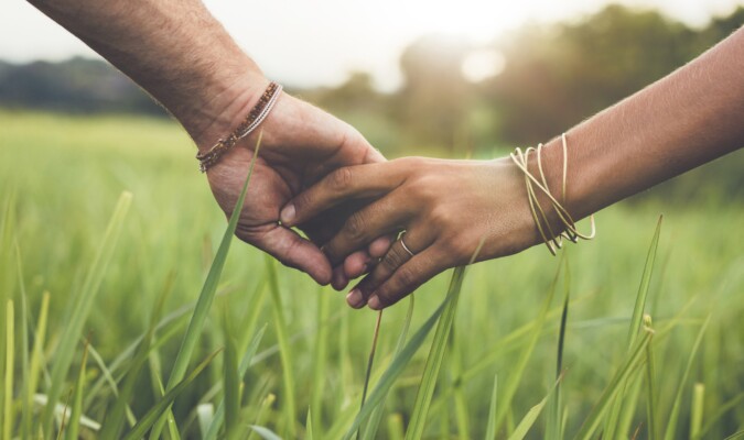 Two hands interlocked with a grassy field in the background.