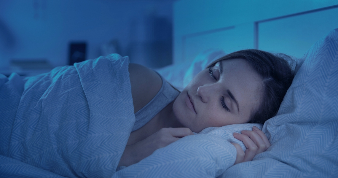 A blue-toned image of a woman sleeping in bed.