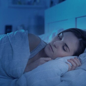 A blue-toned image of a woman sleeping in bed.