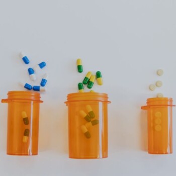 Three orange pill bottles on their side with capsules and tablets spilling out of them.