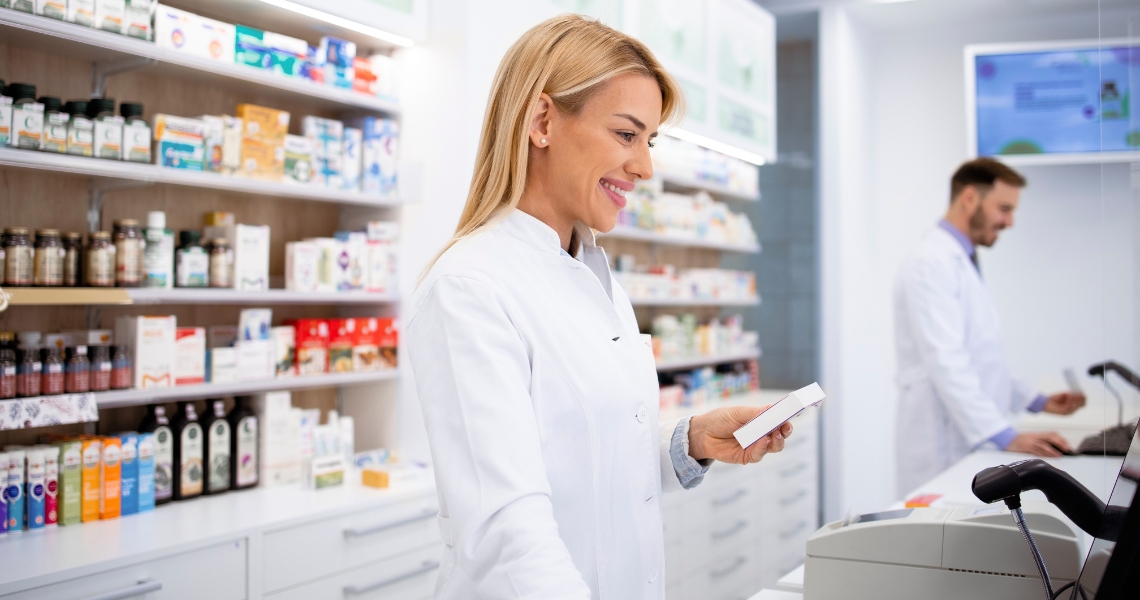 A pharmacist smiling while using a computer and holding a medication.