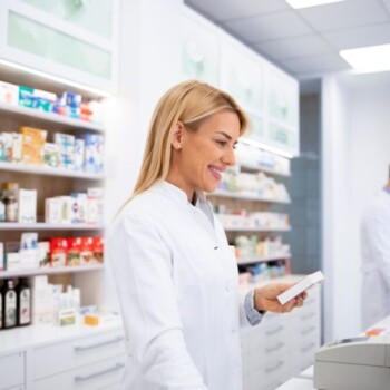 A pharmacist smiling while using a computer and holding a medication.