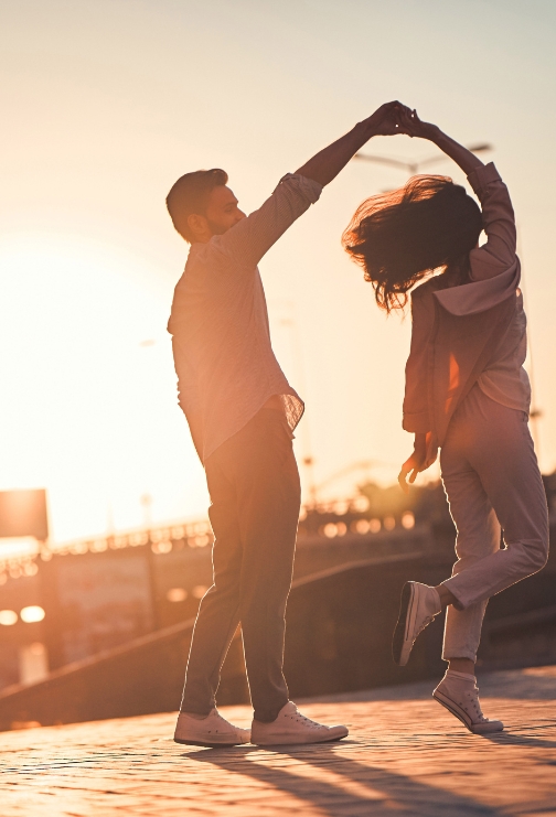 A man and woman dancing outdoors with the sunset in the background.