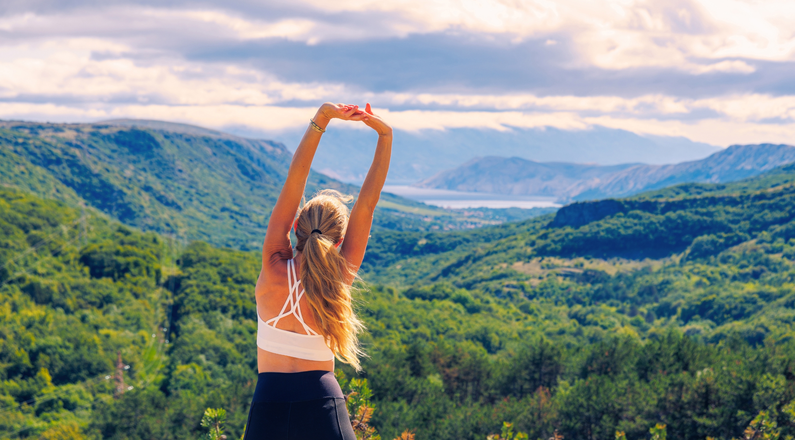 Woman in workout attire stretching facing mountains.