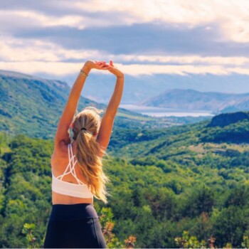 Woman in workout attire stretching facing mountains.