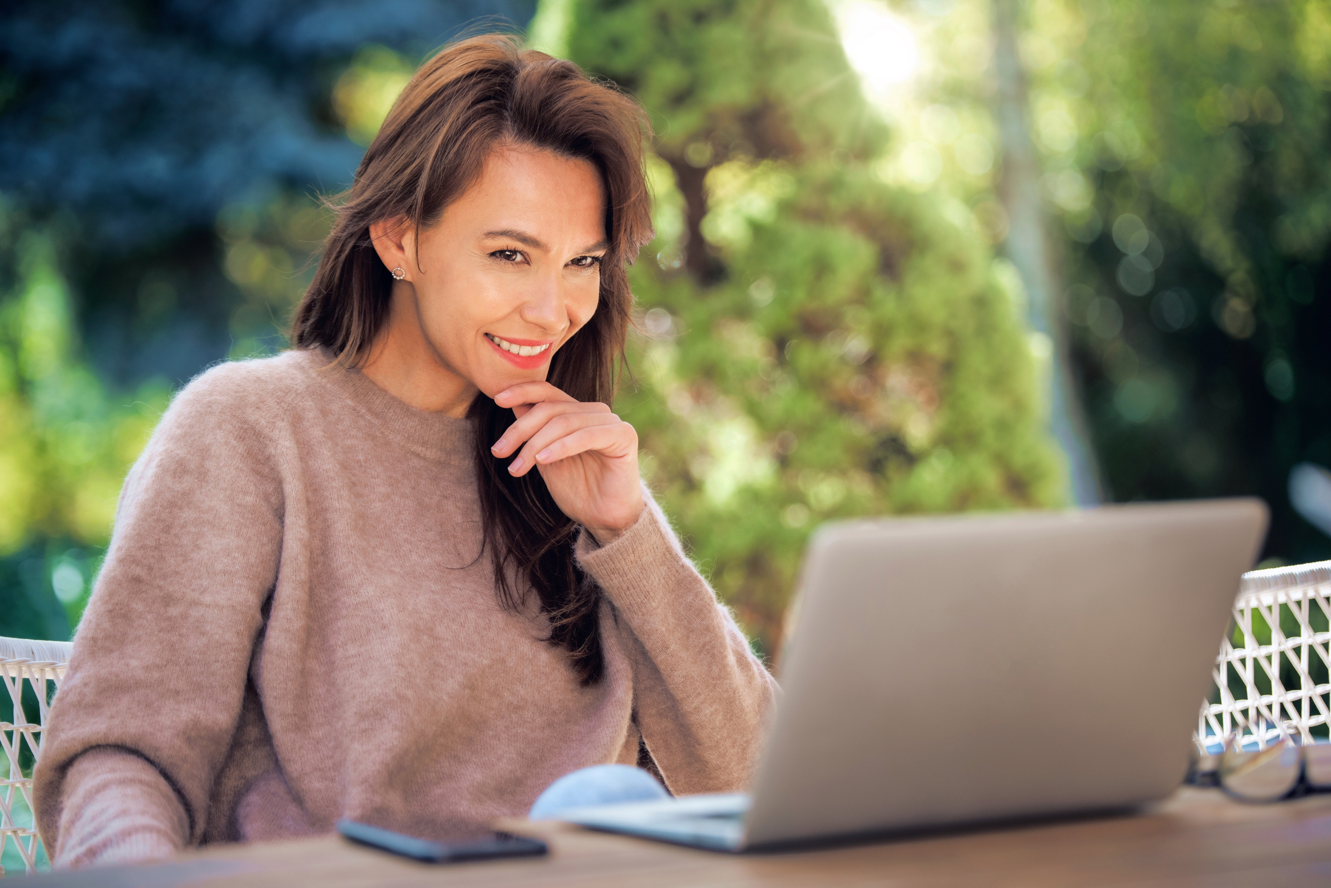 A middle-aged woman with brown hair using her laptop outdoors.