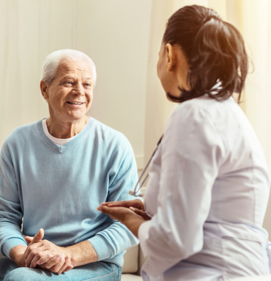 A provider in a white lab coat speaking with an older male patient.