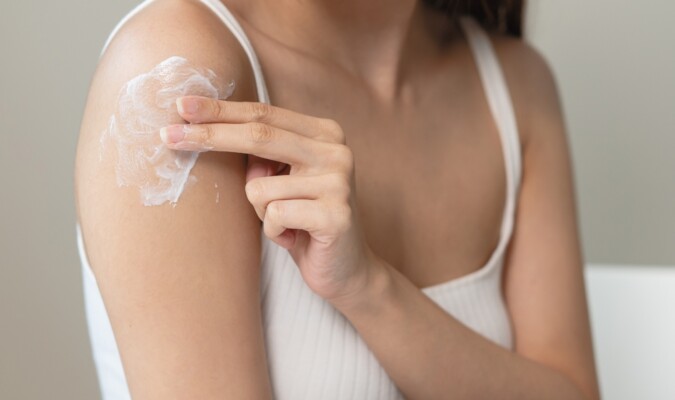 A person applying white cream to their shoulder.