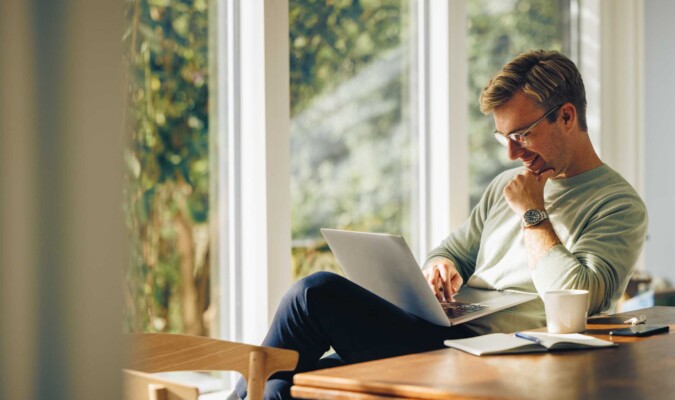 A man sitting inside in the sun on his laptop.