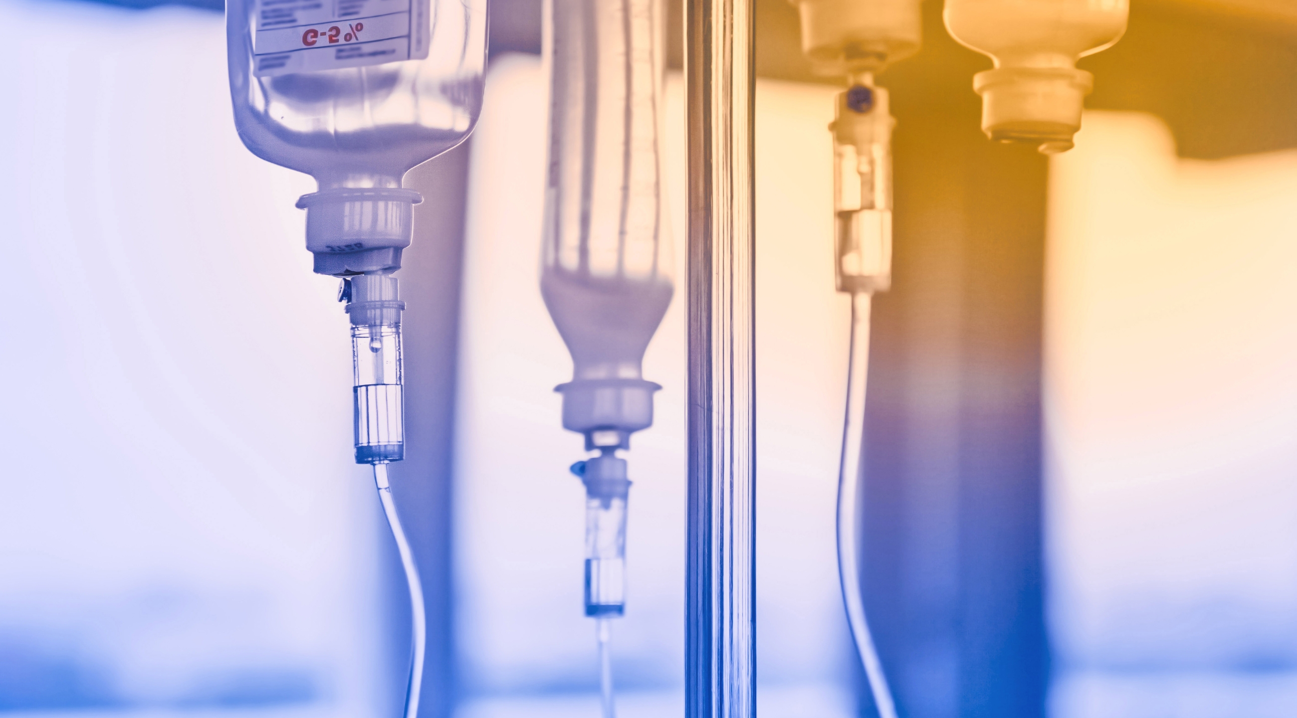 A blue and orange toned image displaying IV bags hanging on an IV pole.