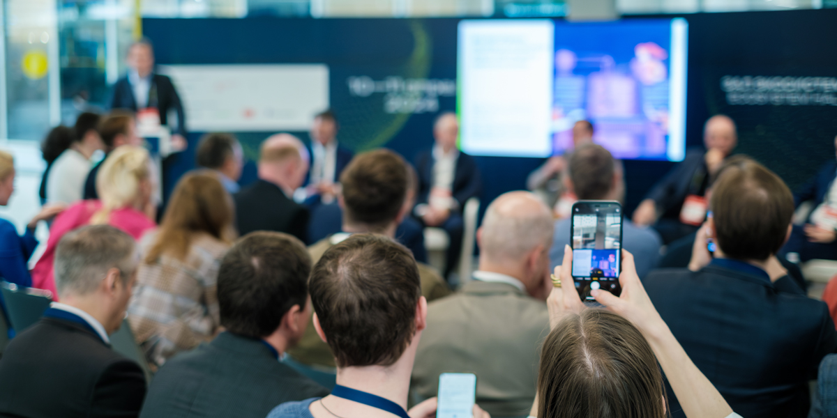 A person in a crowd taking a picture of a presentation