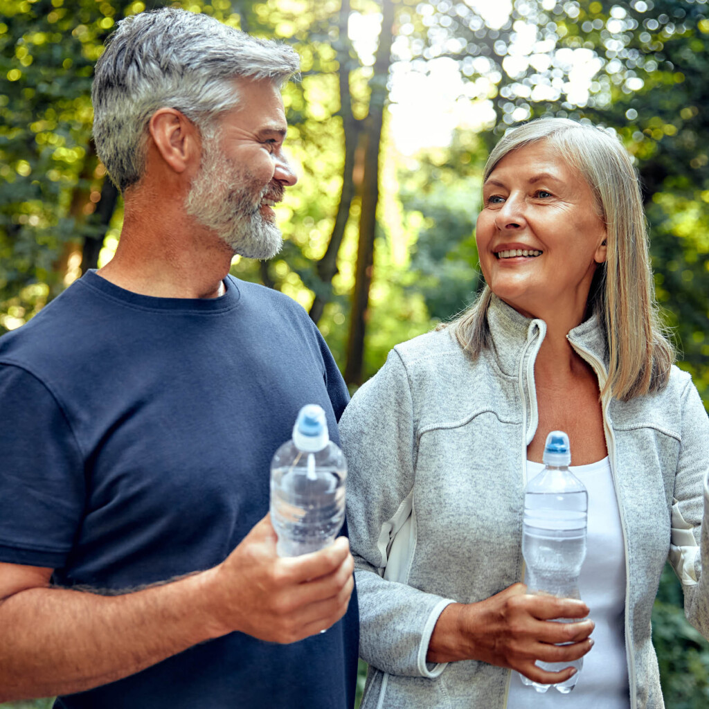 empower-pharmacy-longevity-600×600-2025-2 older couple hiking in woods holding water bottles