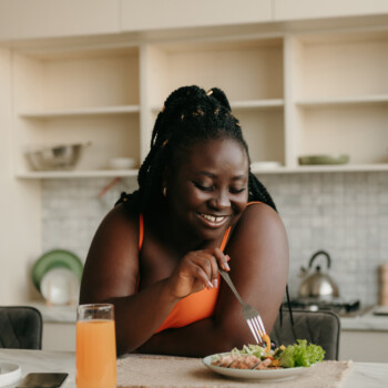 woman eating on kitchen counter with a glass of OJ next to the plate
