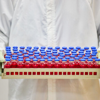 Vials of medicine in a tray being held by two gloved hands