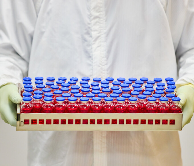 Vials of medicine in a tray being held by two gloved hands