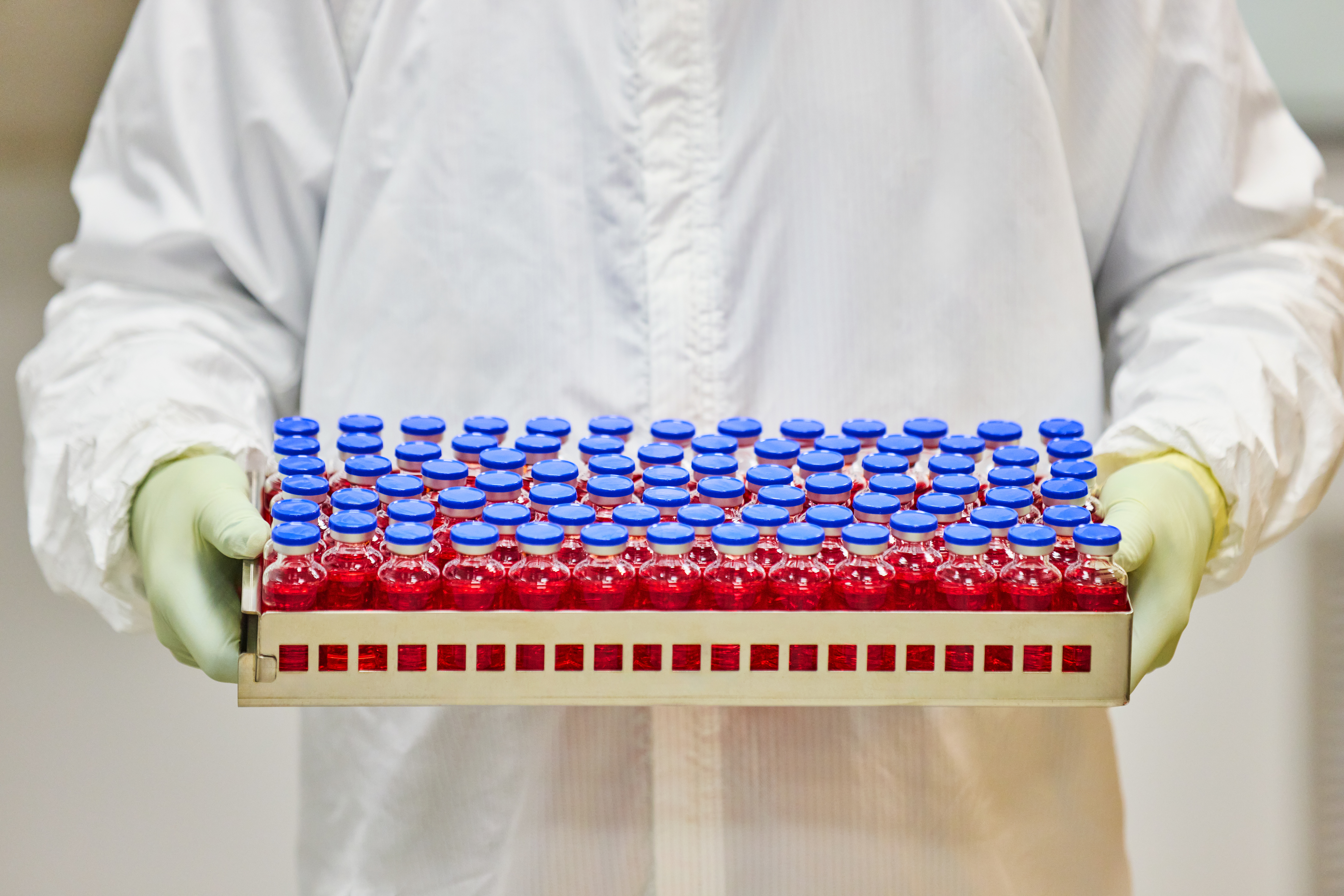 Vials of medicine in a tray being held by two gloved hands